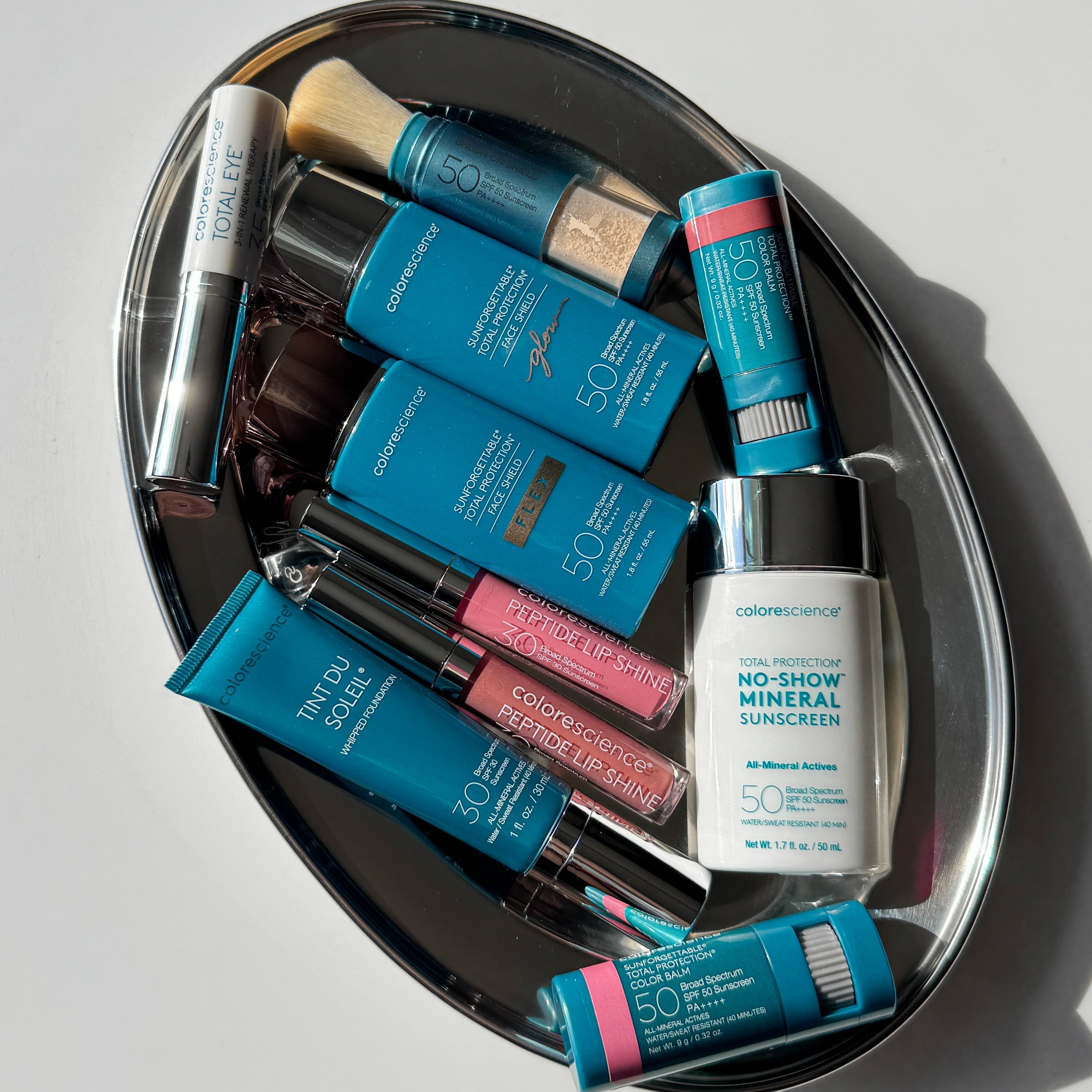 Colorescience products displayed on a wooden table outdoors in the Spring with lush green foliage with white flowers in the background.
