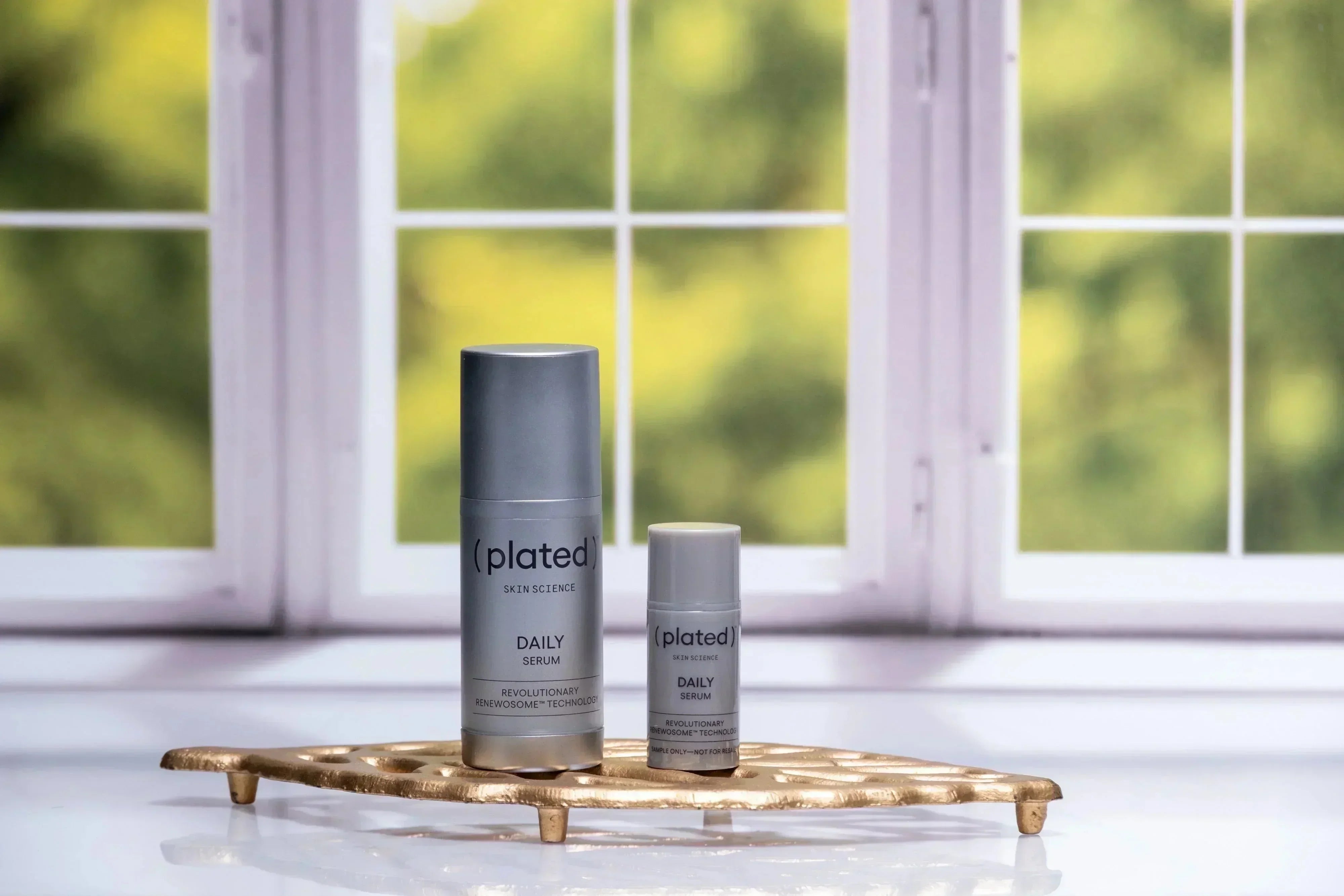 Plated Skin Science daily serum bottles on gold tray by window, skincare product display