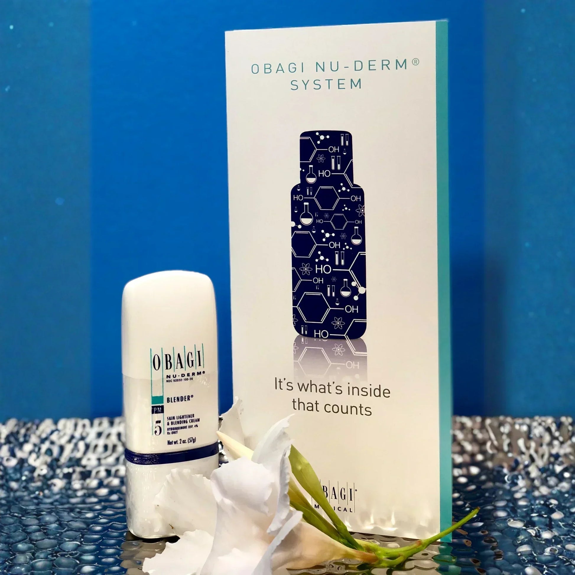 Obagi Nu-Derm Blender bottle and packaging with flower on reflective surface, skincare product