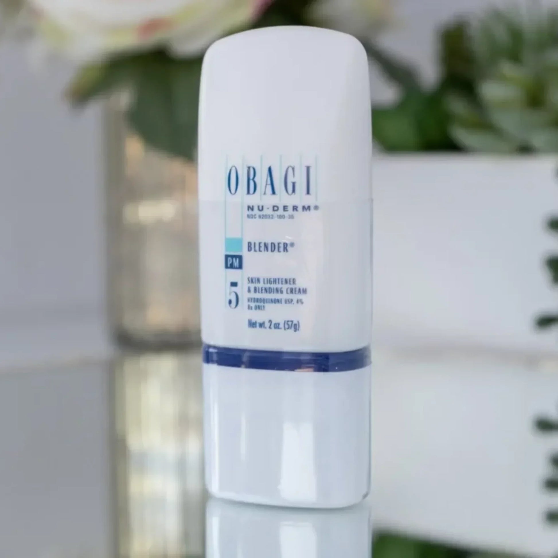 Obagi Nu-Derm Blender skin lightener cream bottle on reflective surface with plants in background