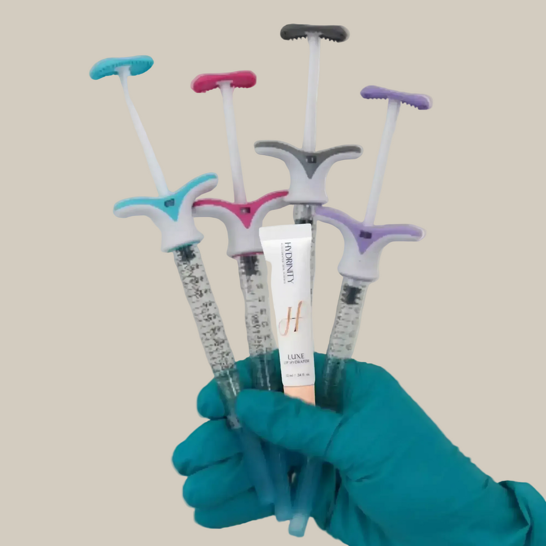 A gloved hand holds a Hydrinity Luxe RF Hydrator tube and several colorful facial massage tools.