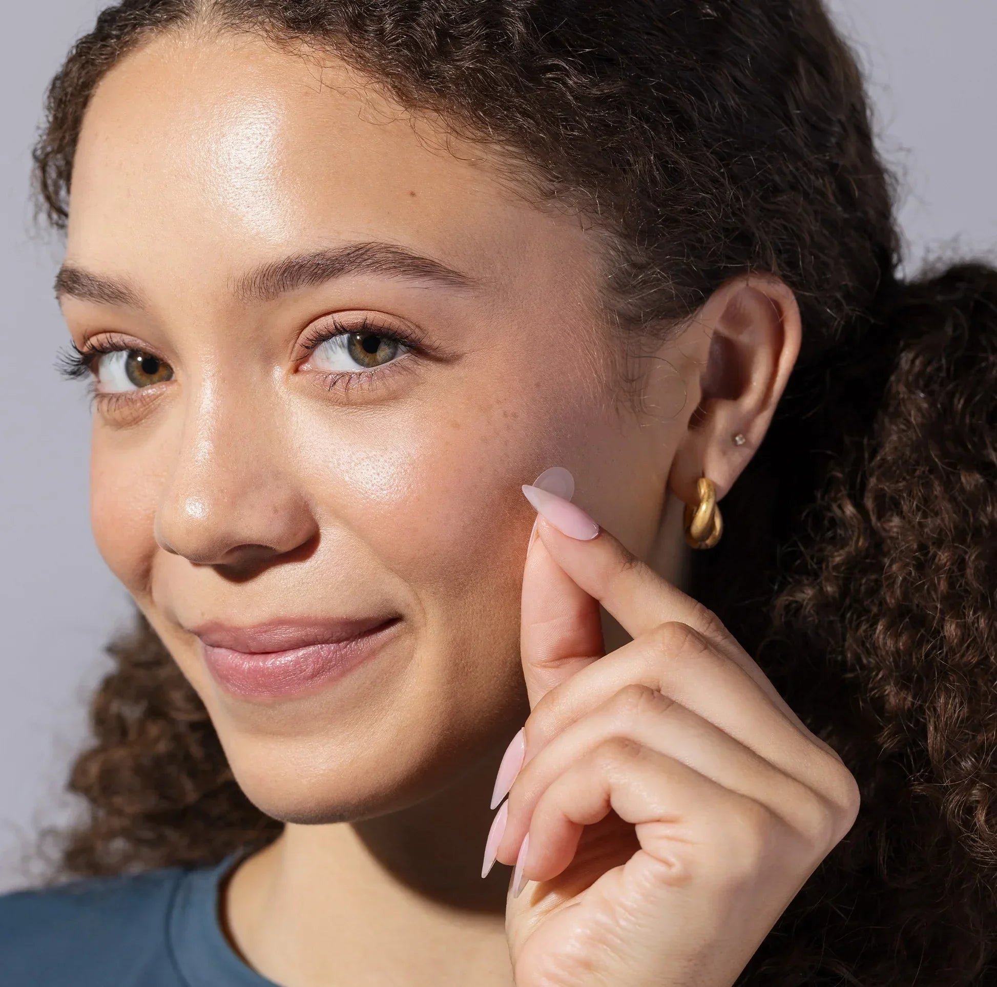 Woman applying clear acne patch to cheek, skincare routine demonstration.