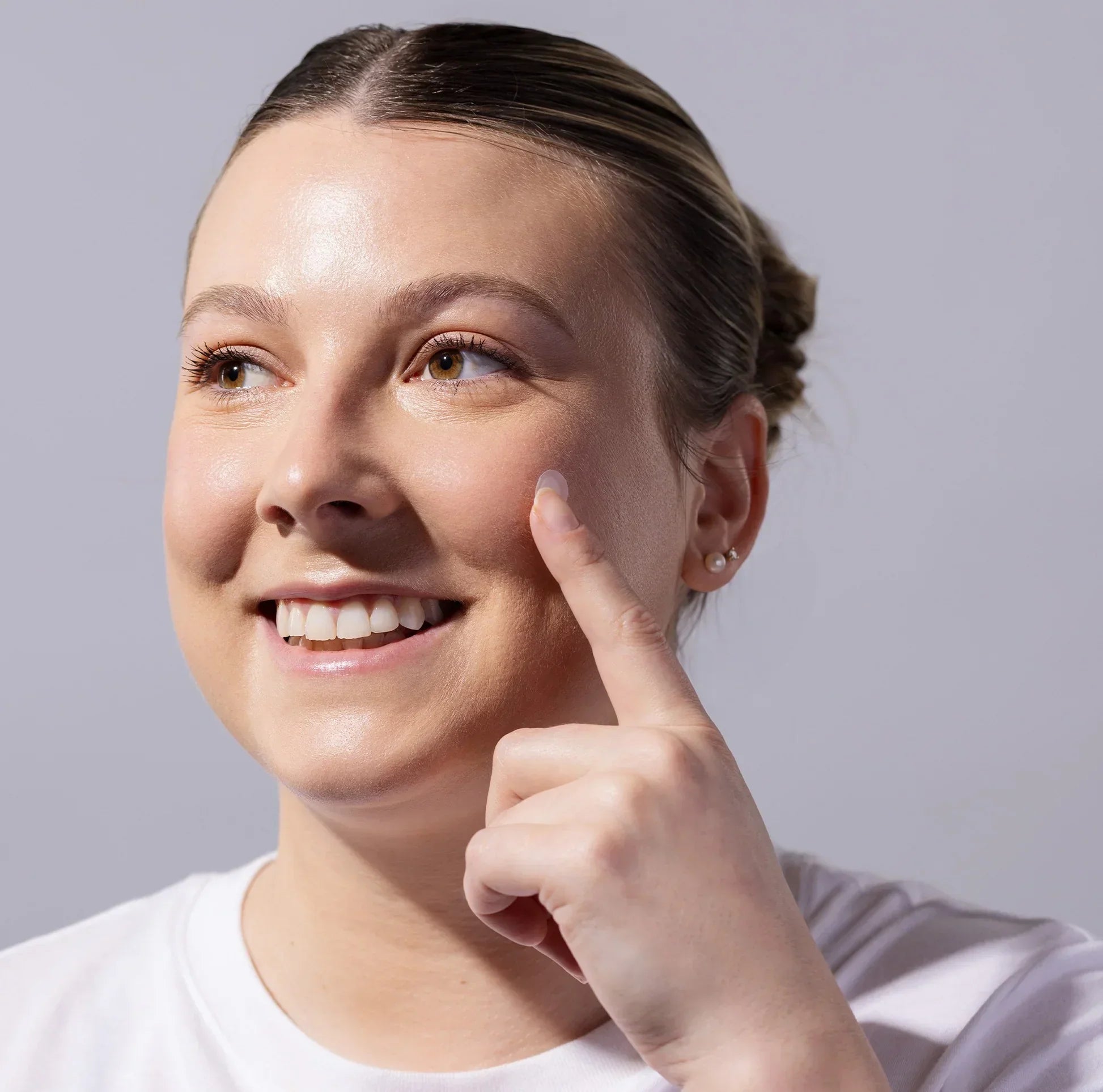 Smiling woman applying skincare product to cheek, healthy glowing skin, close-up shot