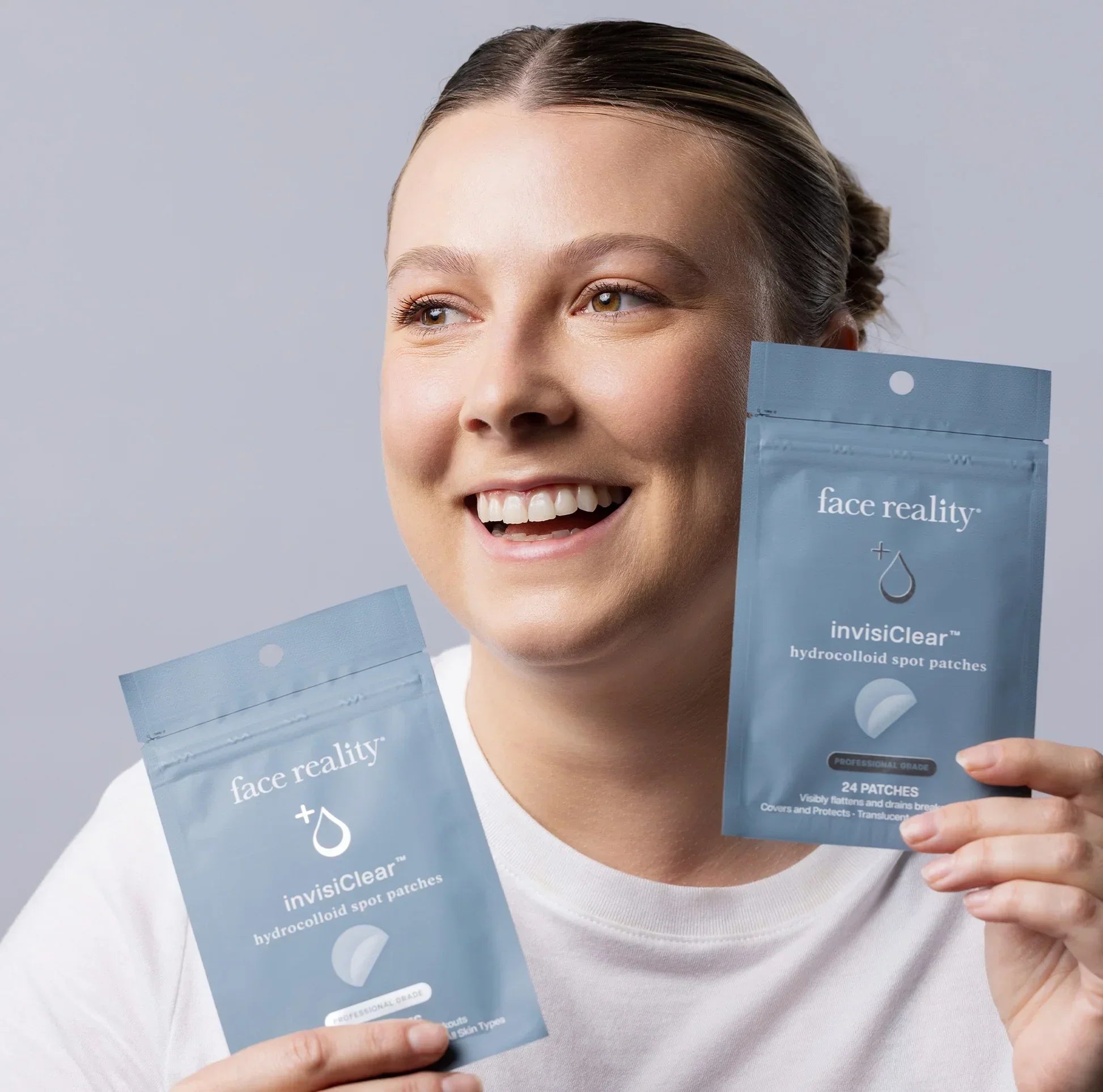 Smiling woman holding two Face Reality InvisiClear hydrocolloid spot patch packages