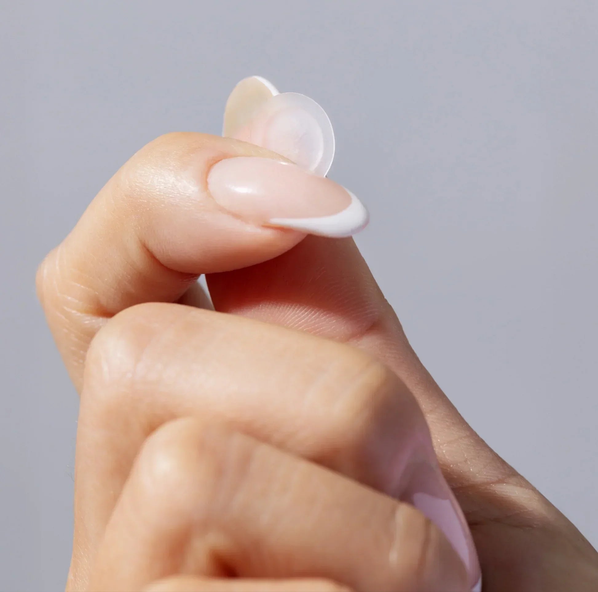 Hand holding a clear acne patch for skincare on a neutral background