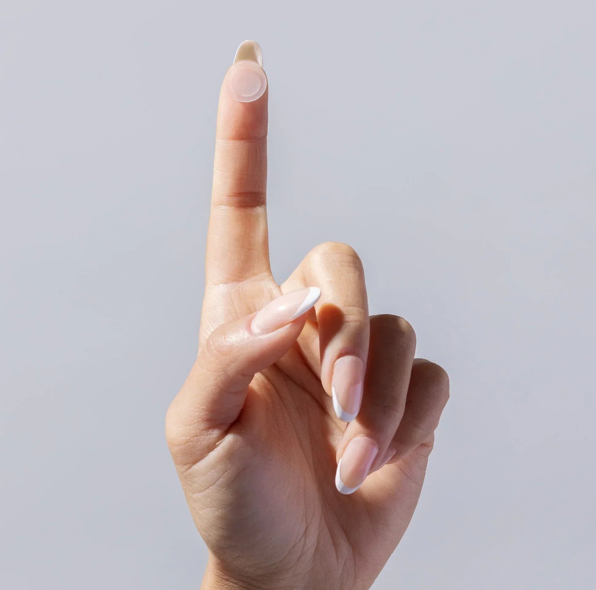 Hand with manicured nails holding a clear acne patch on fingertip against a neutral background.