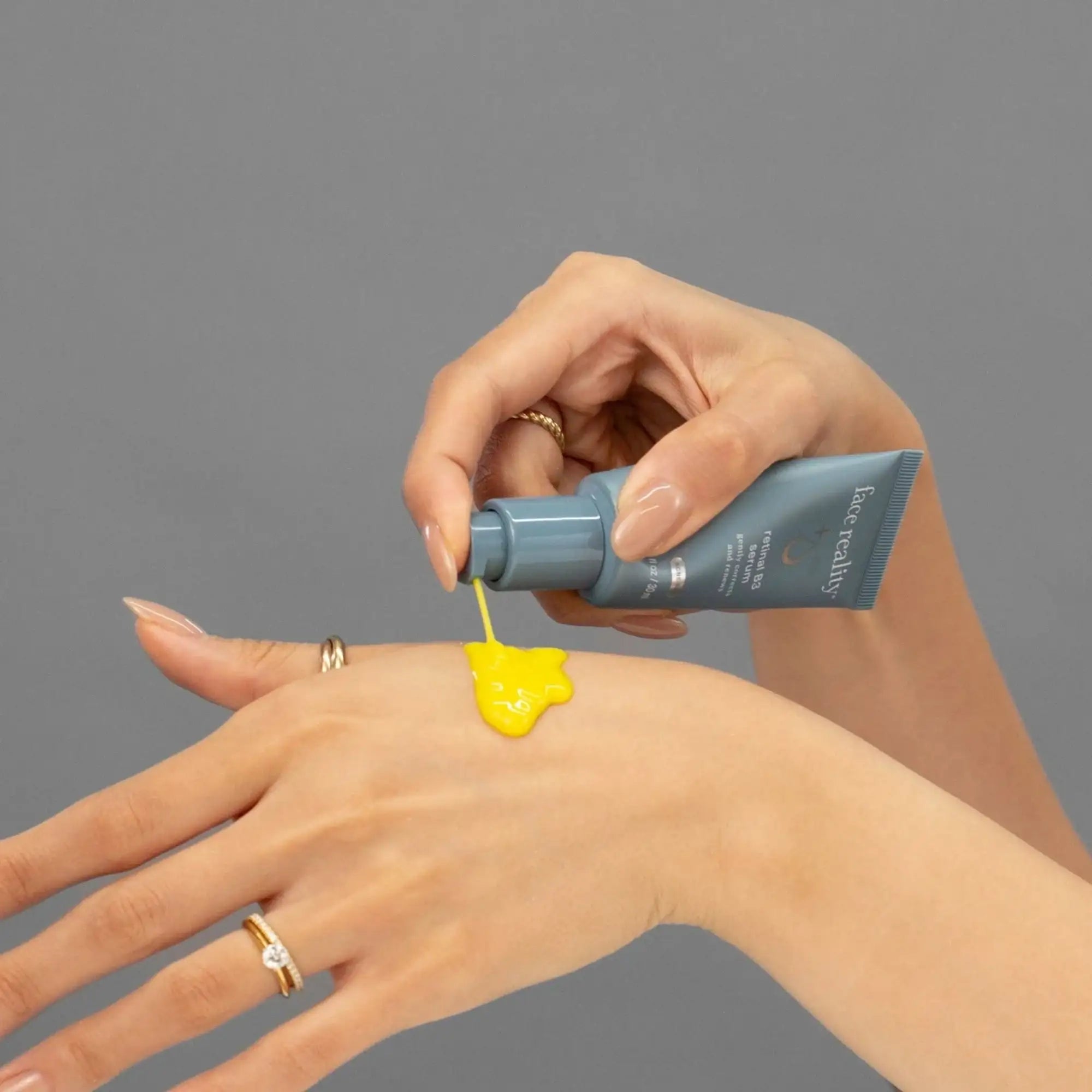 Hand applying yellow Face Reality skincare product on skin against gray background