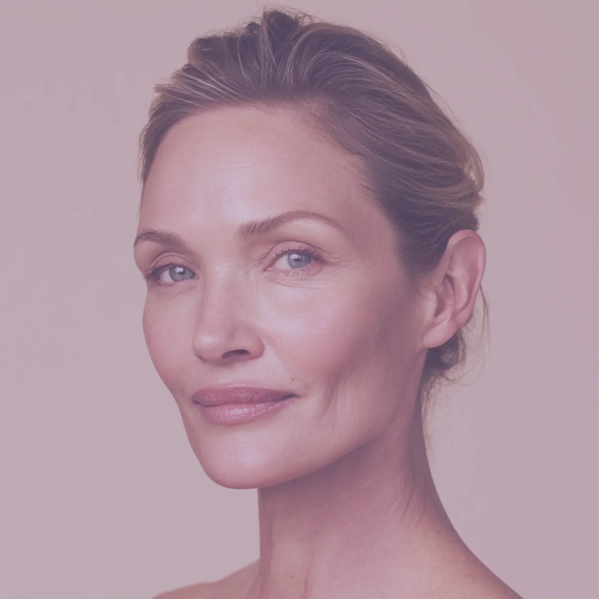 Mature woman with healthy, glowing skin against a soft beige background, skincare focus