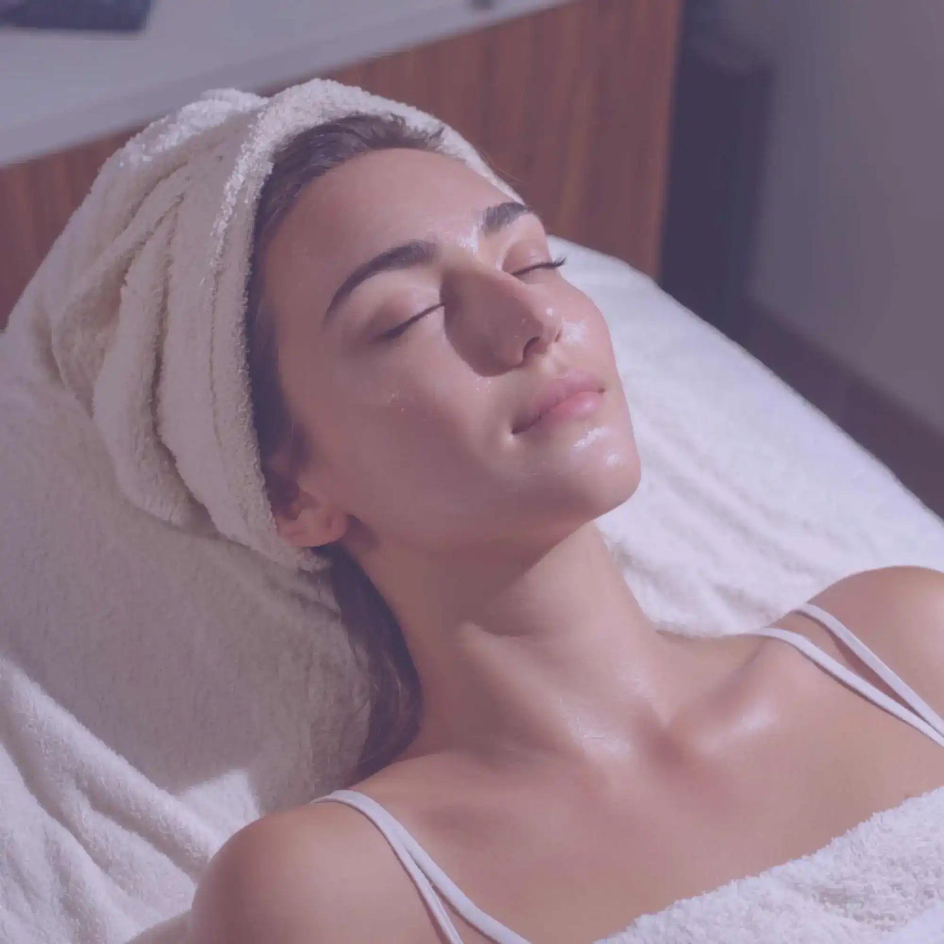 Woman relaxing with towel headwrap during skincare spa facial treatment