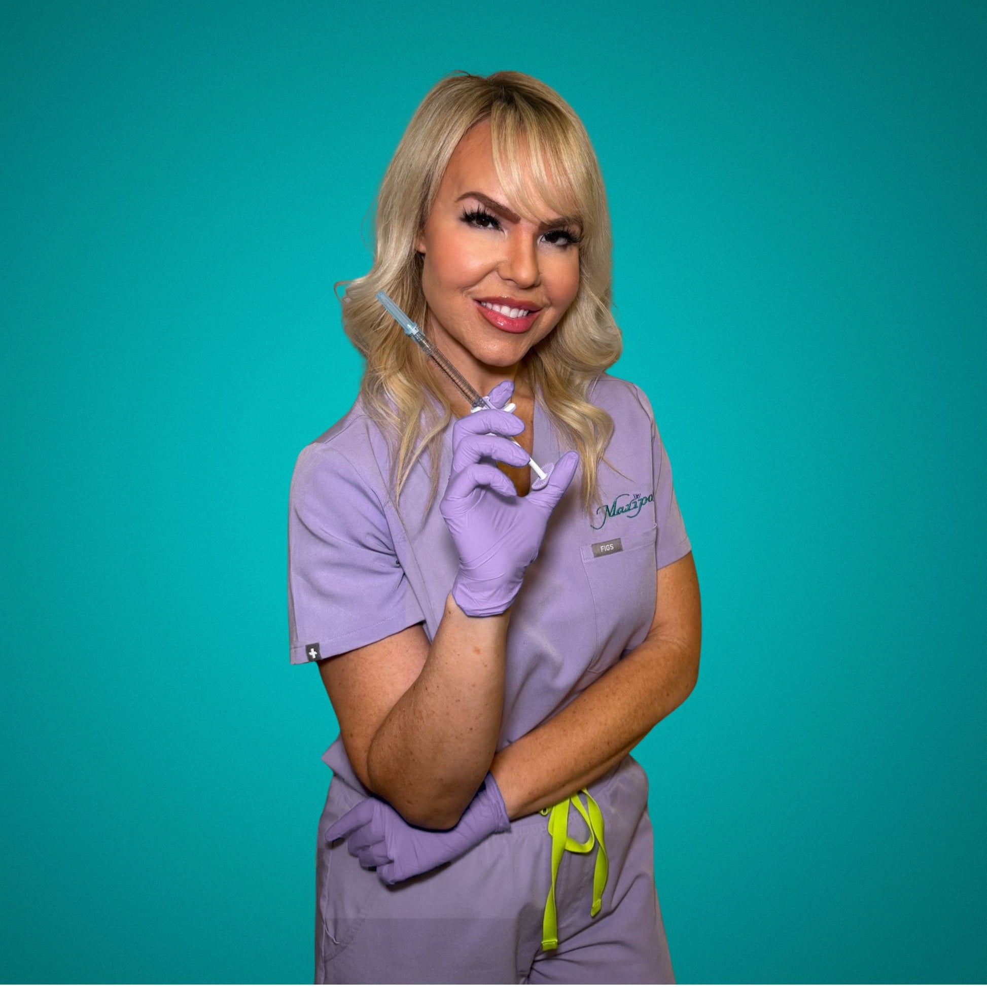 Smiling female skincare clinician with blonde hair holding syringe, wearing purple scrubs and gloves