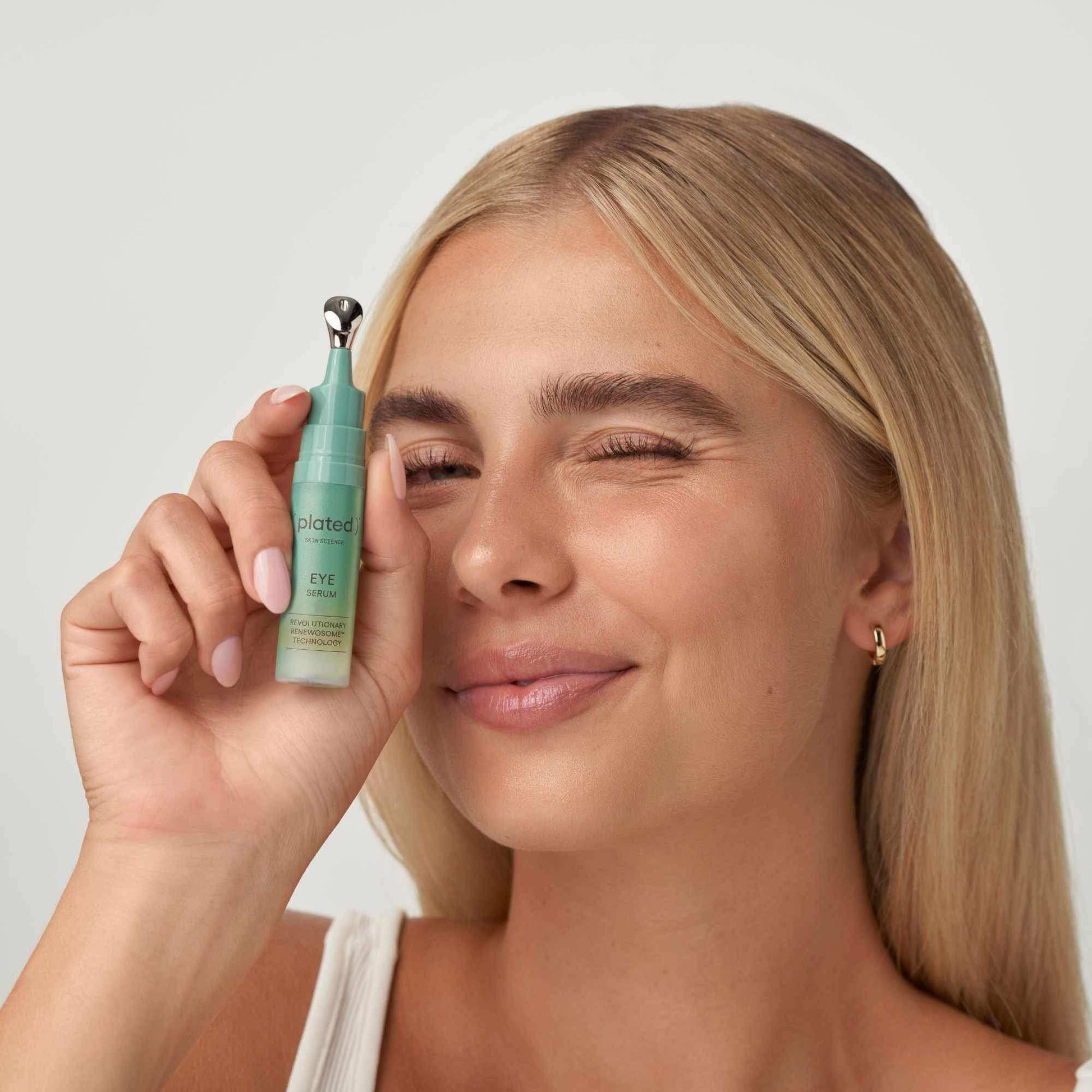 Woman holding Plated Skin Science Eye Serum with applicator, showcasing skincare product.