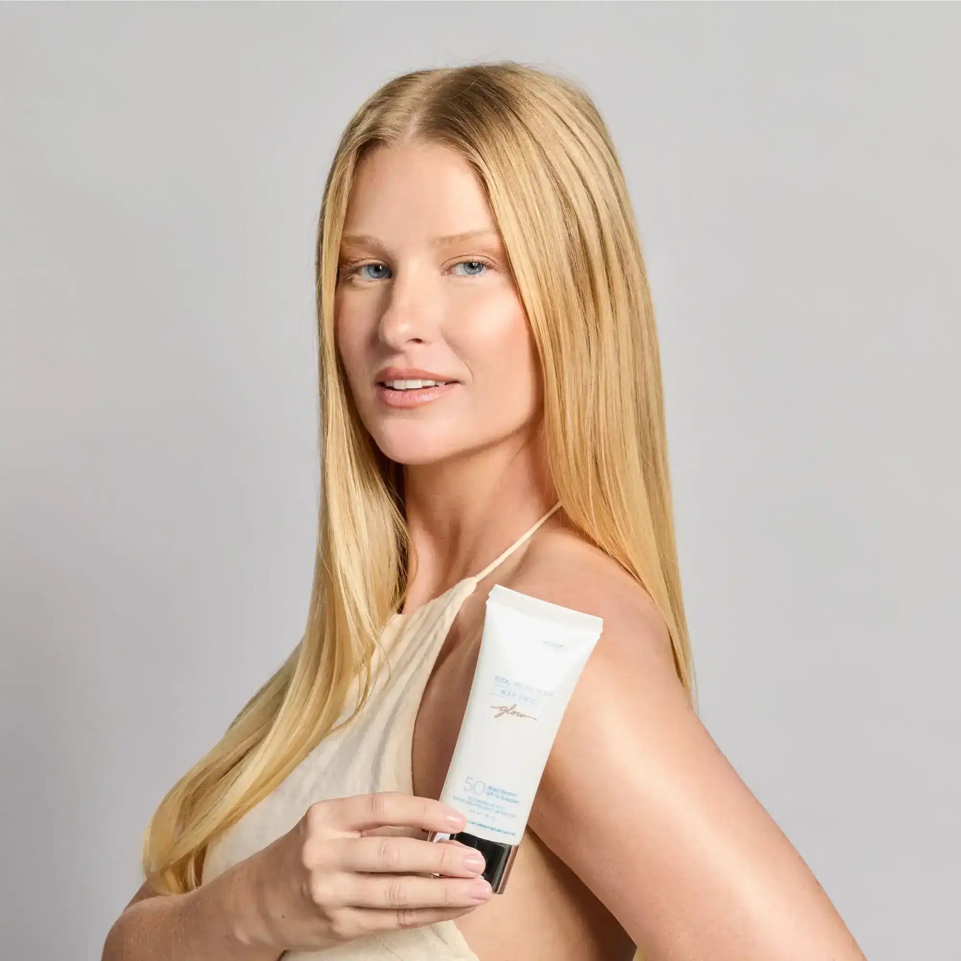 Woman holding SPF 50 sunscreen for radiant skin glow