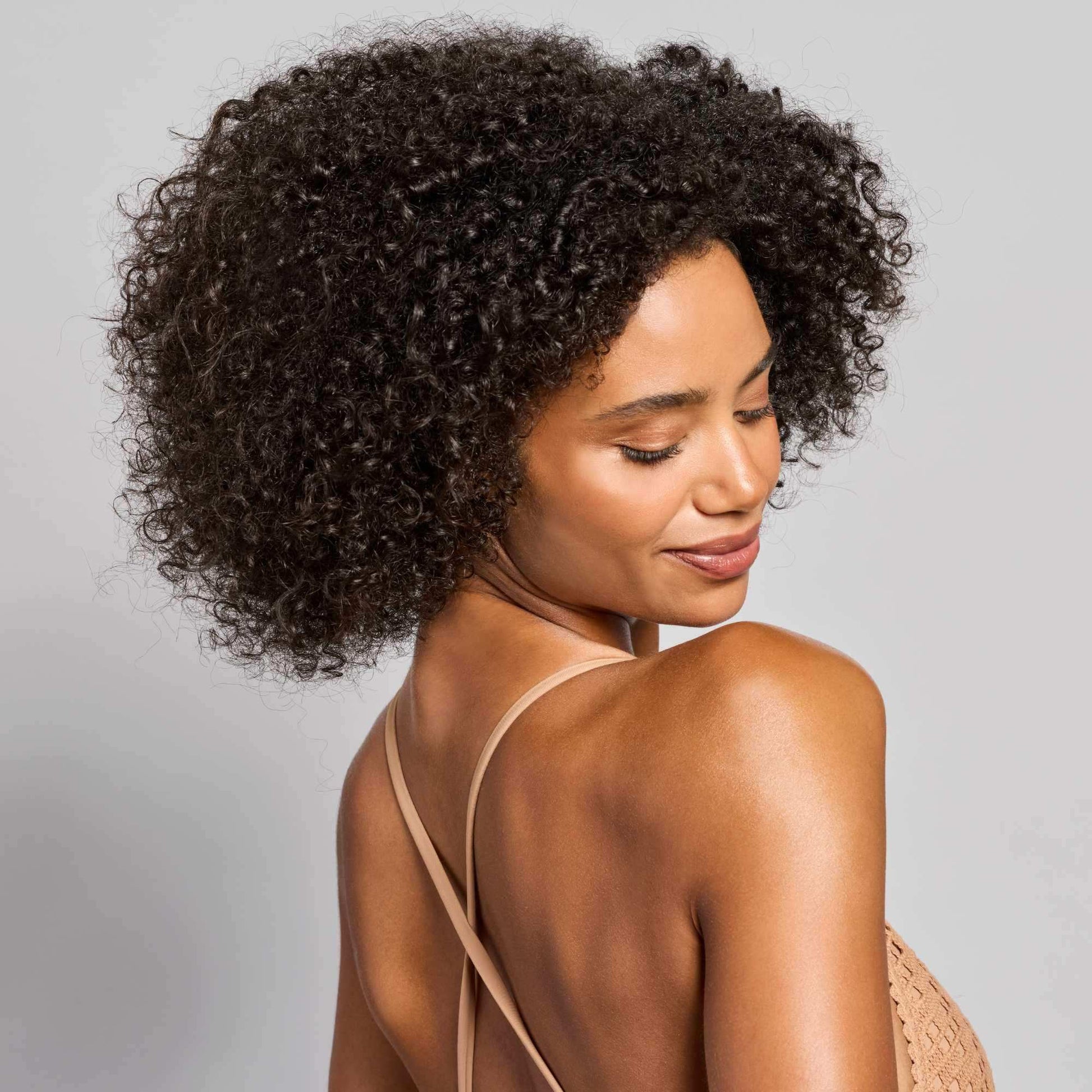 Woman with curly hair and glowing skin, showcasing natural beauty and wellness