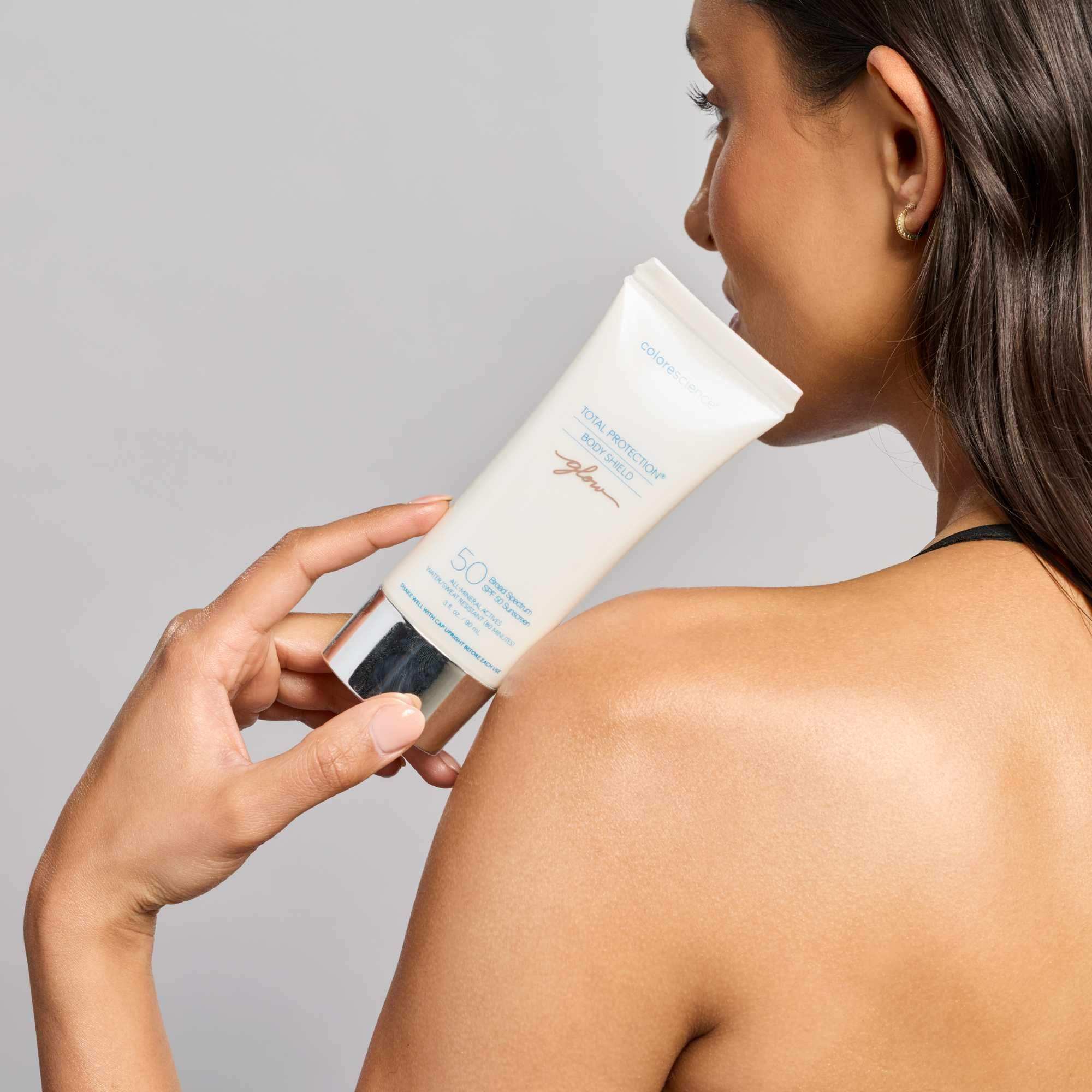 Woman applying Colorescience Total Protection Body Shield SPF 50 sunscreen to shoulder