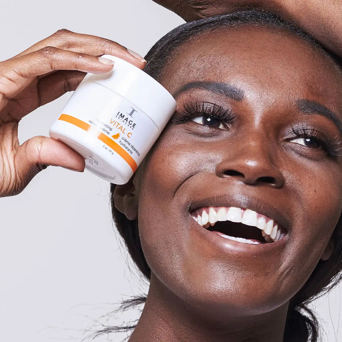 Smiling woman holding IMAGE Vital C hydrating repair creme jar near her face